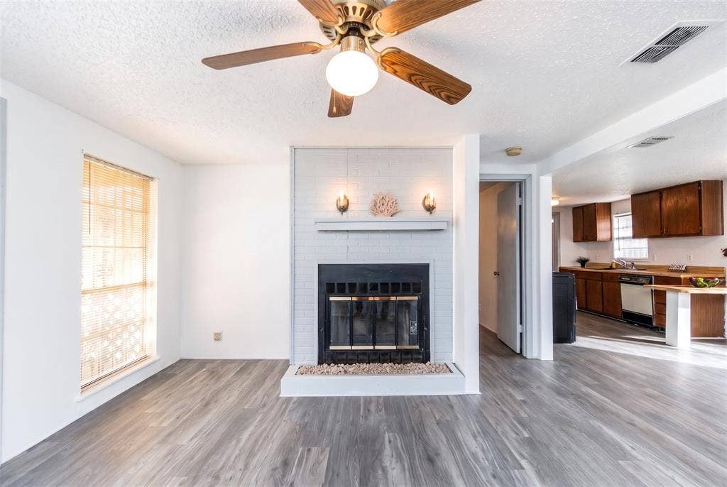 Fireplace with painted brick surround and integrated mantel, wood-finish flooring, and ceiling fan with light fixture