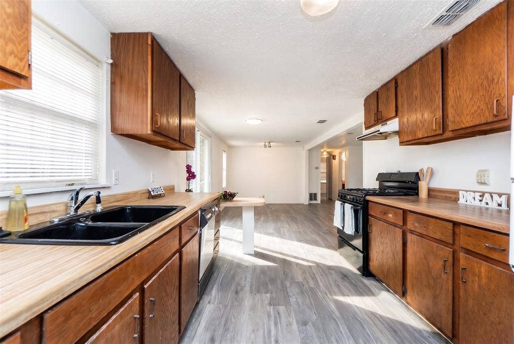 Kitchen featuring wood cabinetry, laminate countertops, double-basin sink, and wood-finish flooring
