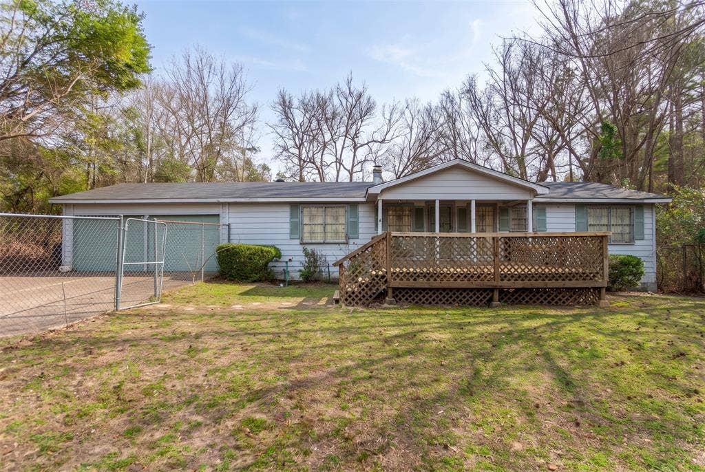 Single-story residence featuring lap siding, a wooden front deck with lattice skirting, an attached two-car garage, and a chain-link fenced perimeter