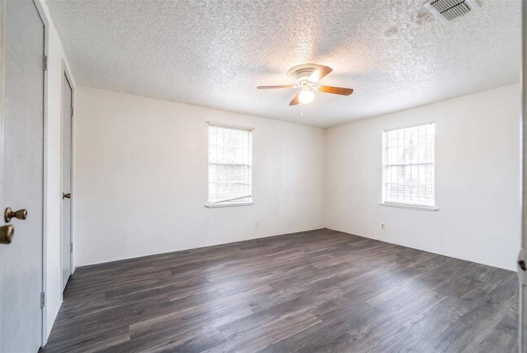 Interior room featuring wood-finish flooring, two dual-pane windows with metal security bars, and a ceiling-mounted light fixture with a fan