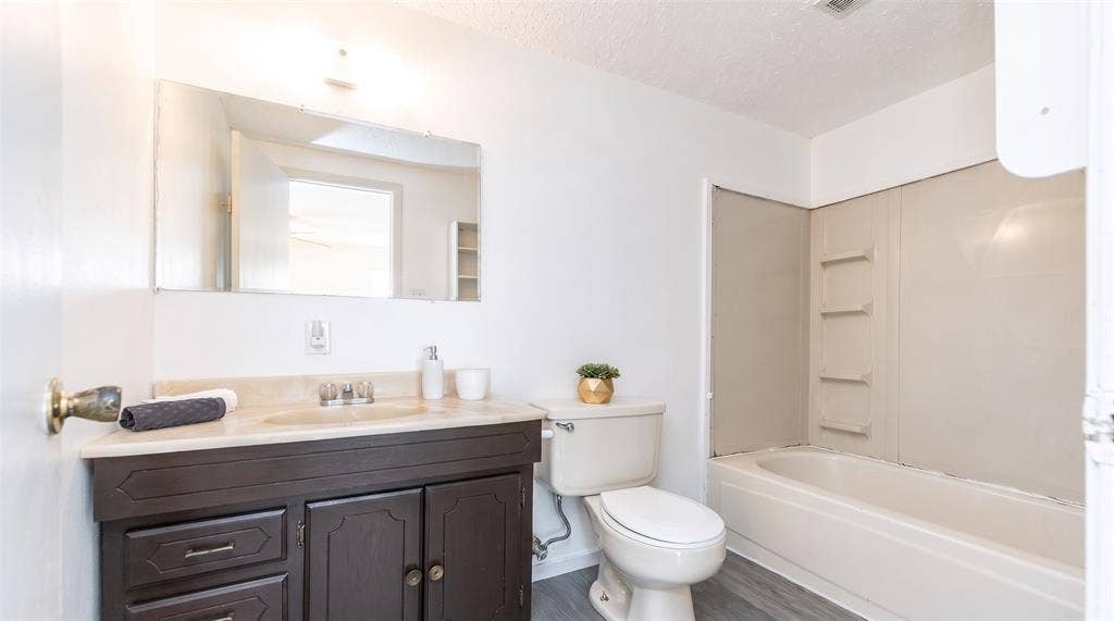 Bathroom featuring a dark wood-finish vanity, stone-surface countertop with an integrated basin, wall-mounted mirror, and a tub-shower combination with surround panels