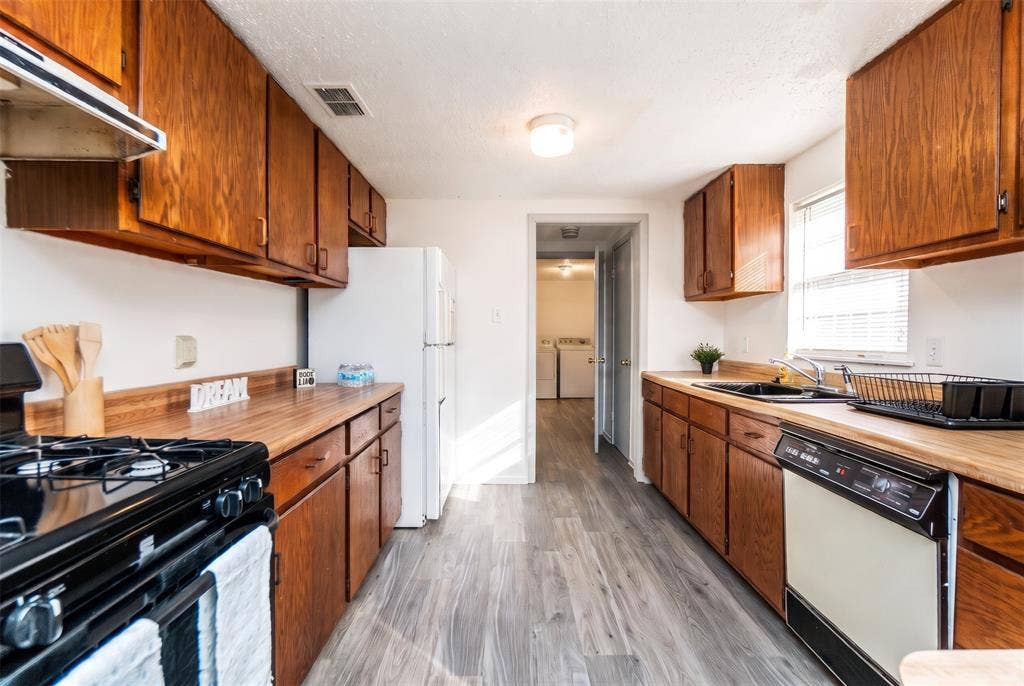 Kitchen featuring wood cabinetry, butcher block-style countertops, wood-finish flooring, and a stainless steel gas range