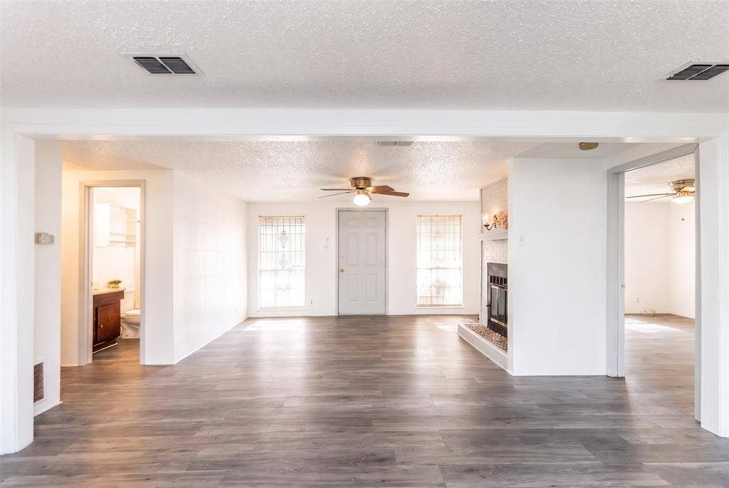 Open-concept area featuring wood-finish flooring, a painted brick fireplace with a raised hearth, and neutral wall tones
