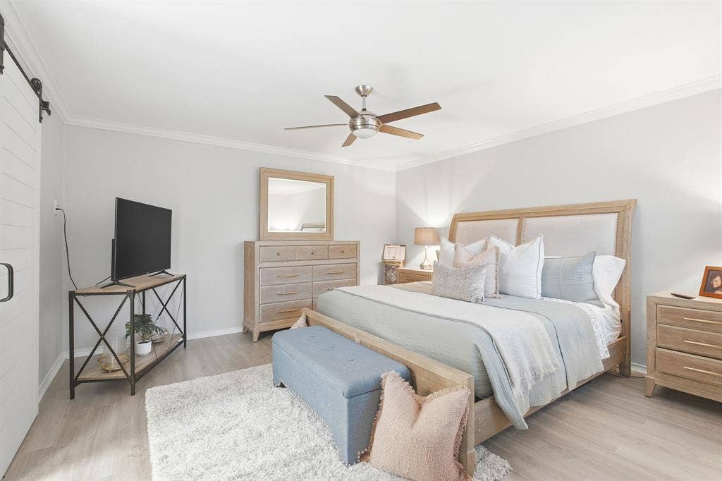 17365 Remington Park Circle, Dallas, TX 75252 Room featuring light wood-finish flooring, white sliding barn door with black hardware, and a ceiling fan with integrated lighting