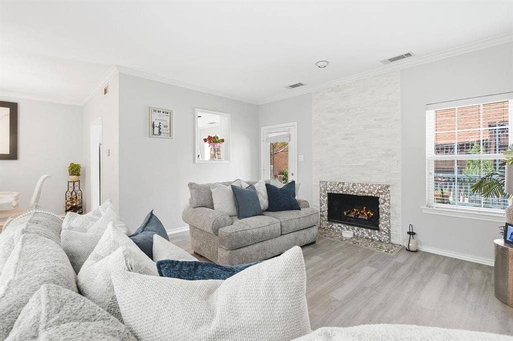 17365 Remington Park Circle, Dallas, TX 75252 Living area featuring wood-finish flooring, a fireplace with a stacked-stone surround, decorative pebble-tile hearth, and a window with white casing