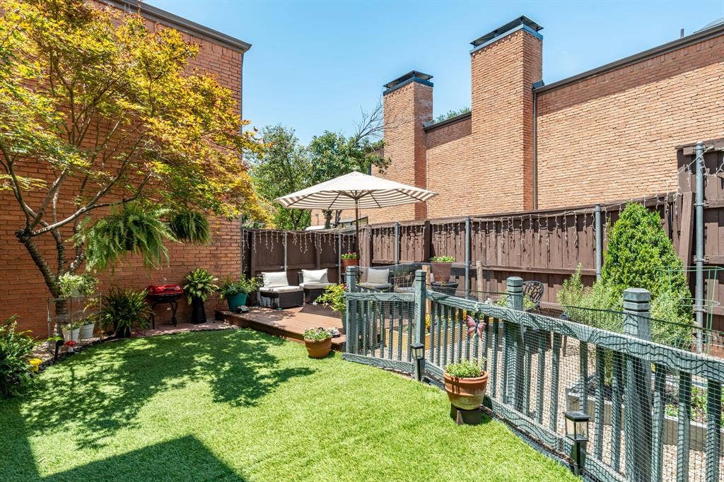 17365 Remington Park Circle, Dallas, TX 75252 Fenced backyard featuring synthetic turf, wood-finish decking, mature trees, and brick exterior walls