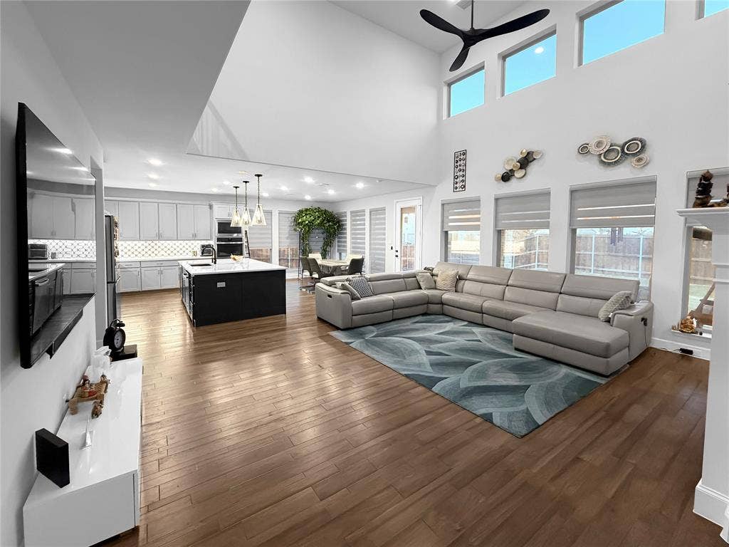 2251 Macy Way, Prosper, TX 75078 Open-concept interior featuring double-height ceilings, wood-finish flooring, a kitchen island with stone countertops, recessed lighting, and large windows with roller shades