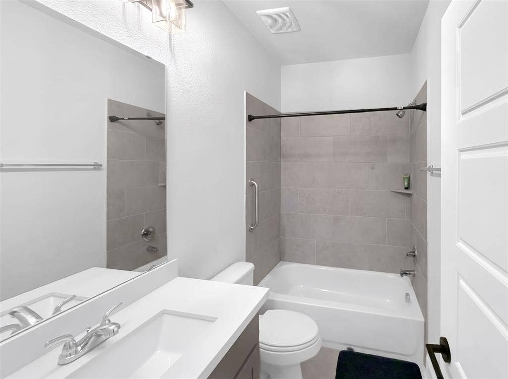 2251 Macy Way, Prosper, TX 75078 Bathroom featuring a vanity with a white rectangular sink and light-toned countertop, a frameless wall mirror, a bathtub with neutral tile surround, and a metal safety grab bar