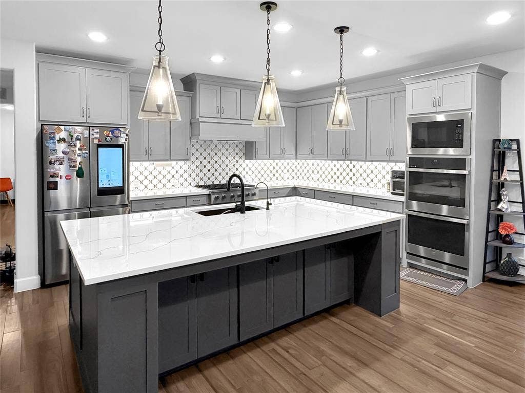 2251 Macy Way, Prosper, TX 75078 Kitchen featuring a central island with quartz countertop, grey shaker-style cabinetry, stainless steel double wall oven, geometric patterned backsplash, and three pendant lights