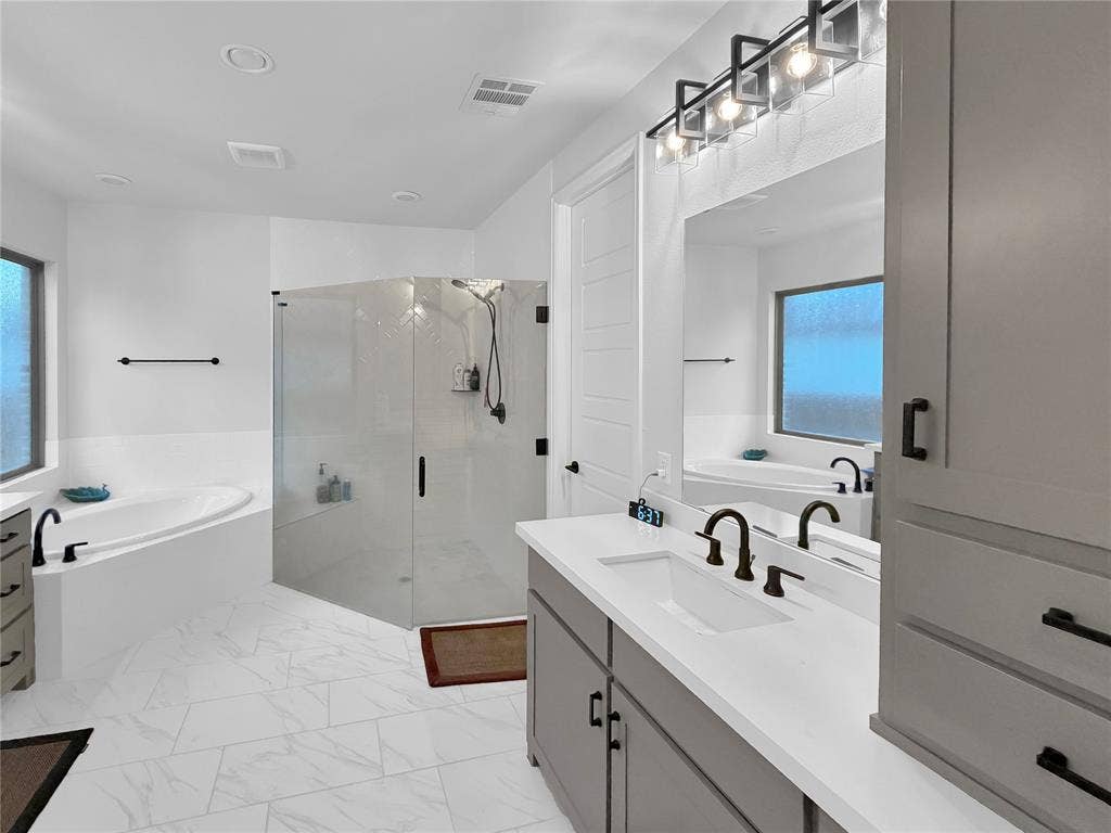 2251 Macy Way, Prosper, TX 75078 Bathroom featuring a dual-sink vanity with stone-composite countertops, a glass-enclosed walk-in shower, a soaking tub, and tile flooring
