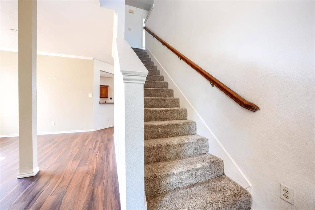 2709 Maci Court, Seagoville, TX 75159 Carpeted staircase featuring a wood-finish handrail and white wall-mounted balustrade, complemented by wood-finish flooring and a structural column