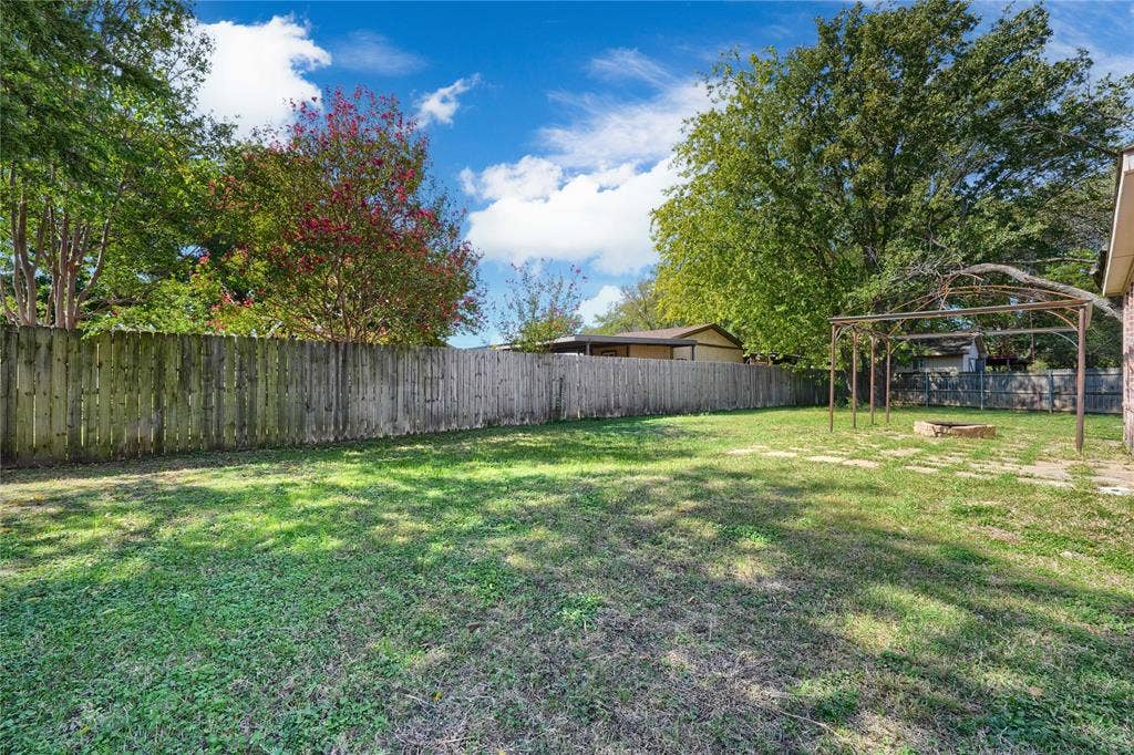 2709 Maci Court, Seagoville, TX 75159 Backyard featuring an expansive lawn, wooden privacy fencing, a metal-frame arbor, and mature trees