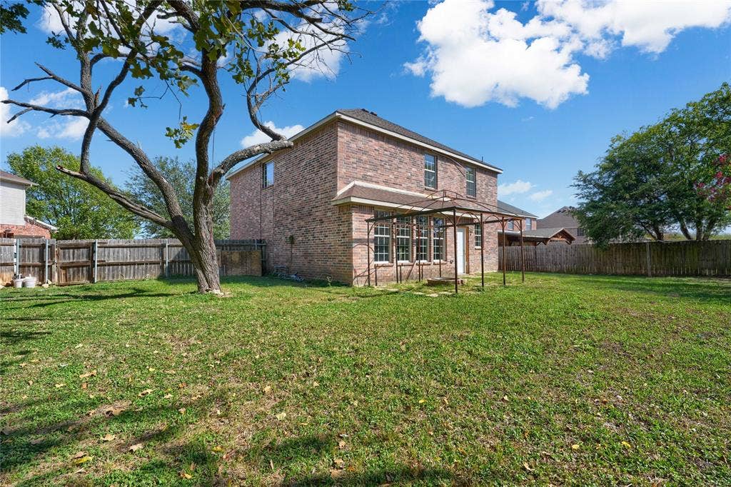 2709 Maci Court, Seagoville, TX 75159 Brick exterior property featuring a large backyard, mature trees, wood privacy fencing, and a metal-frame pergola