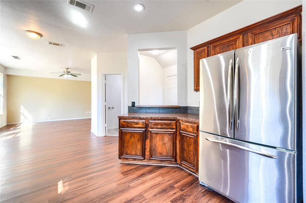 2709 Maci Court, Seagoville, TX 75159 Kitchen featuring stained wood cabinetry, stone-surface countertops, and a built-in stainless steel refrigerator, complemented by wood-finish flooring
