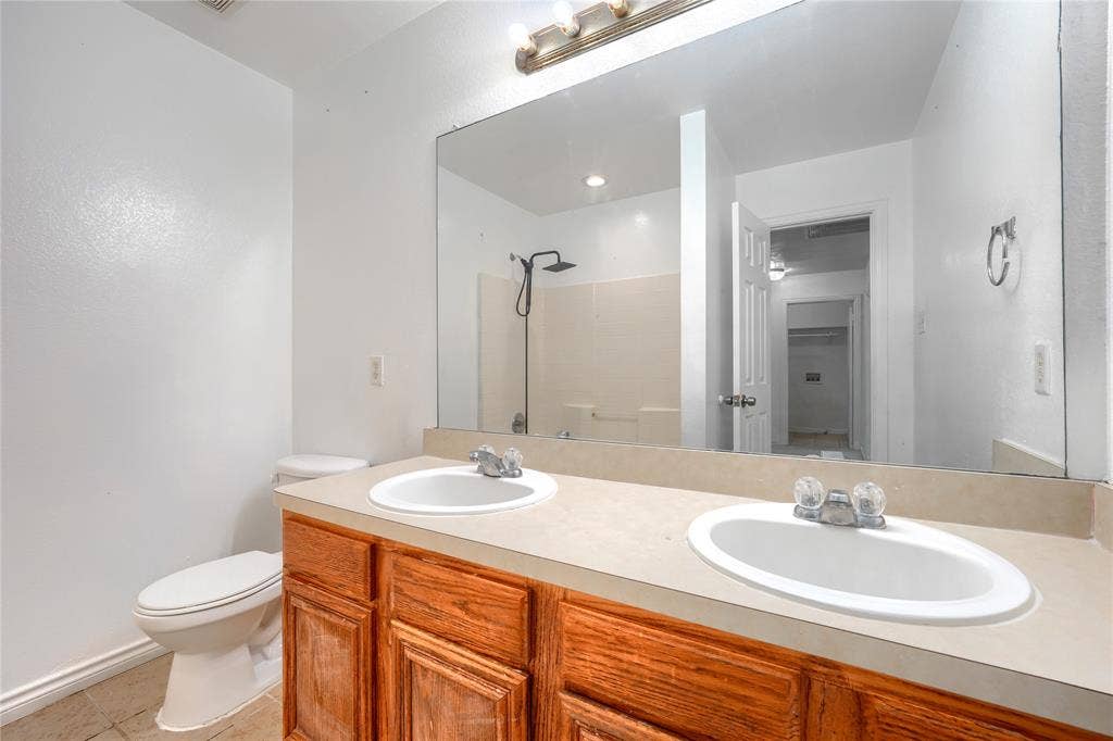 2709 Maci Court, Seagoville, TX 75159 Bathroom featuring a double-sink vanity with wood cabinetry, a solid surface countertop, an expansive wall-mounted mirror, and a walk-in shower