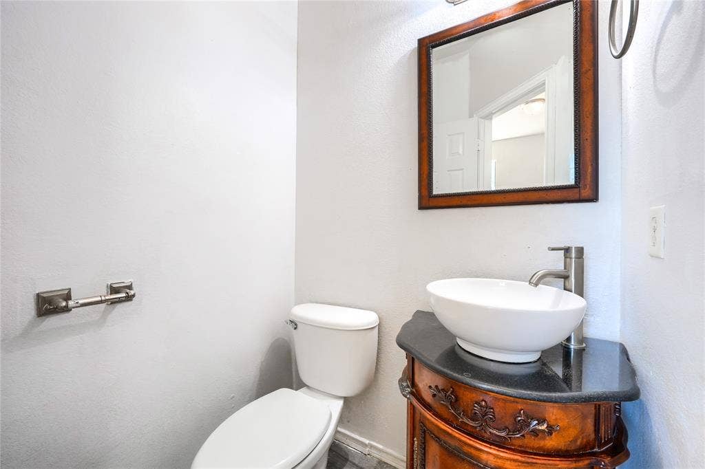 2709 Maci Court, Seagoville, TX 75159 Powder room featuring a wood-finish vanity with ornate detailing, a dark stone countertop, a white oval vessel sink, a brushed-nickel faucet, and a wall-mounted framed mirror