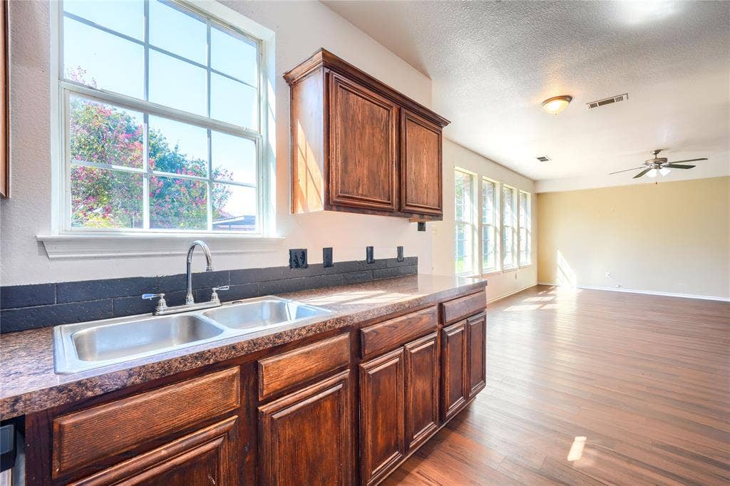 2709 Maci Court, Seagoville, TX 75159 Kitchen featuring dark wood-finish cabinetry, a dual-basin stainless steel sink with a high-arch faucet, a stone-composite countertop, and a dark tile backsplash