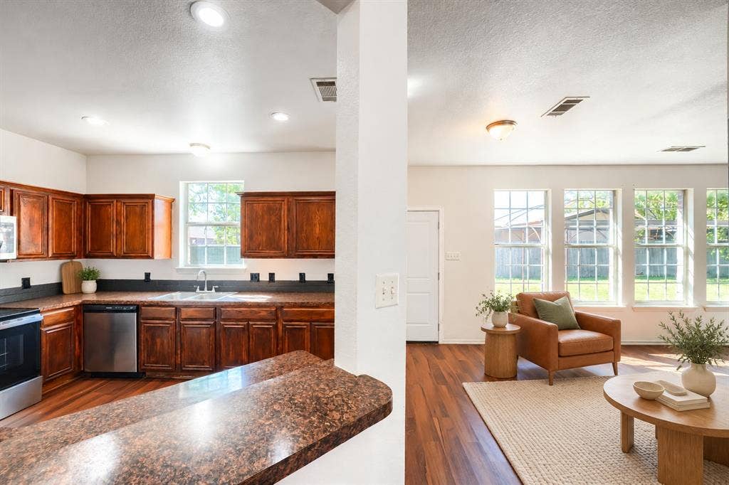2709 Maci Court, Seagoville, TX 75159 Kitchen featuring stained wood cabinetry, stone-finish countertops, stainless steel appliances, wood-finish flooring, and multiple windows