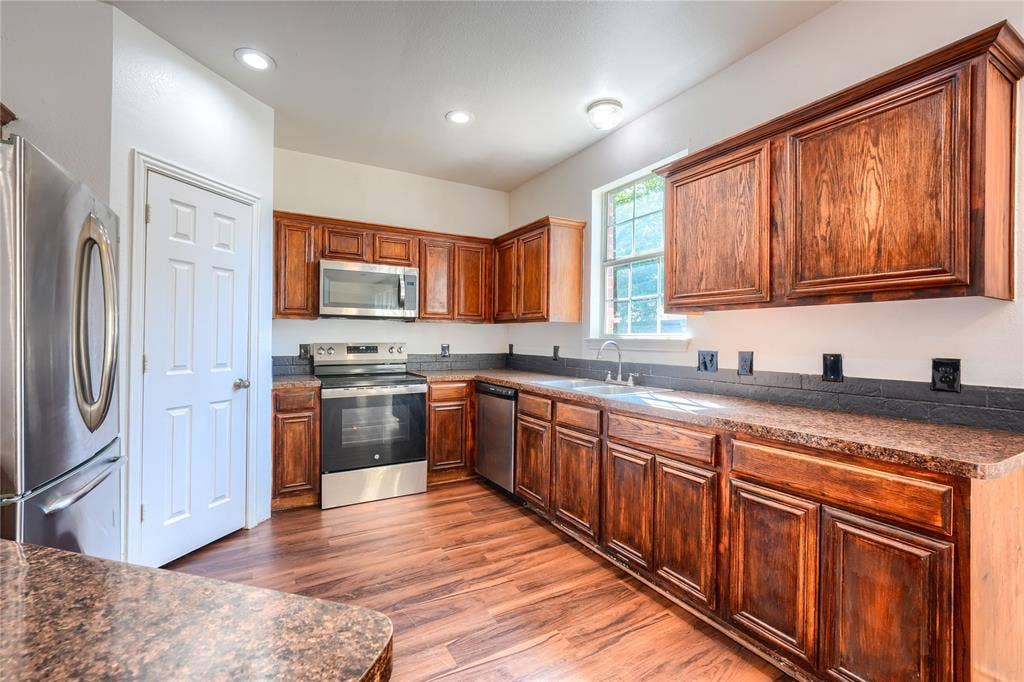 2709 Maci Court, Seagoville, TX 75159 Kitchen featuring rich-toned wood cabinetry, stone-finish countertops, stainless steel appliances, dark tile backsplash, and wood-finish flooring