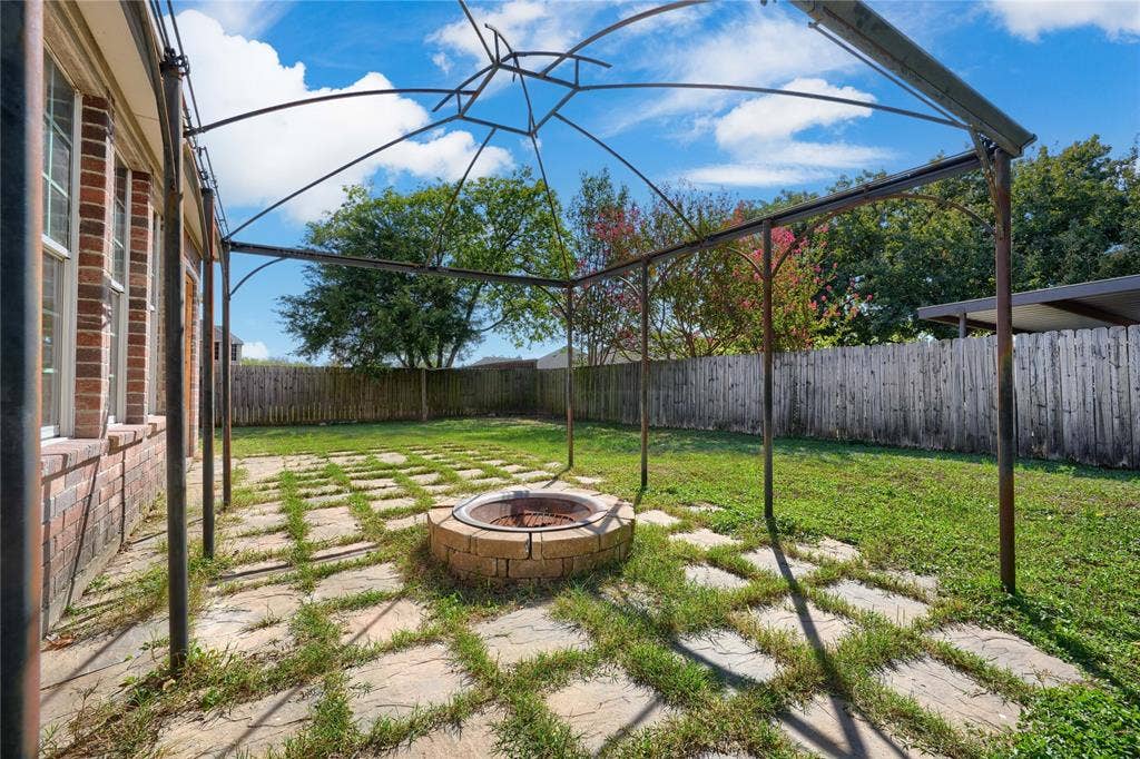 2709 Maci Court, Seagoville, TX 75159 Backyard featuring a metal frame pergola, a circular stone fire pit, grid-patterned stone pavers, and a perimeter wood fence