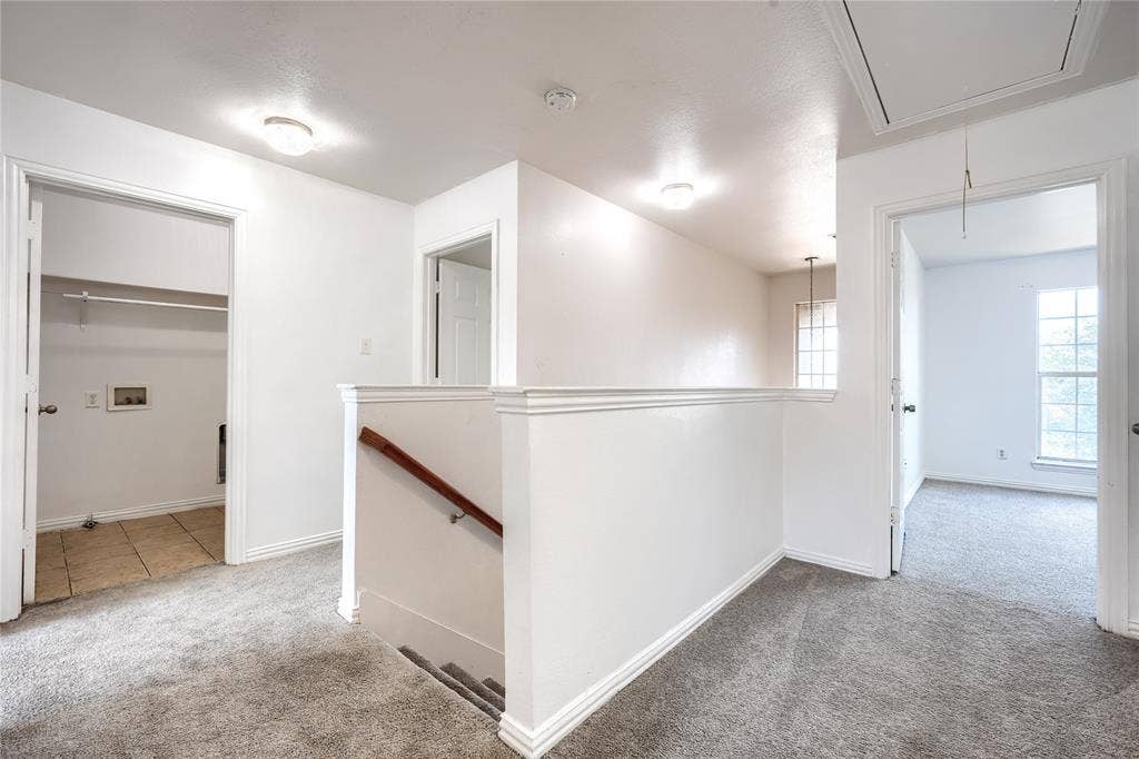2709 Maci Court, Seagoville, TX 75159 Hallway featuring neutral carpeting, a staircase with a wooden handrail, flush-mount ceiling lighting, and multiple interior doorways