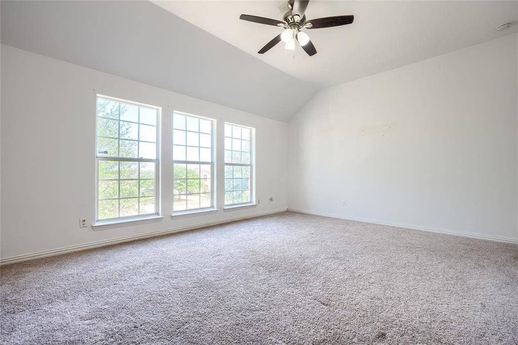 2709 Maci Court, Seagoville, TX 75159 Vaulted ceilings featuring a multi-light ceiling fan and three large grid-pattern windows with neutral carpeting