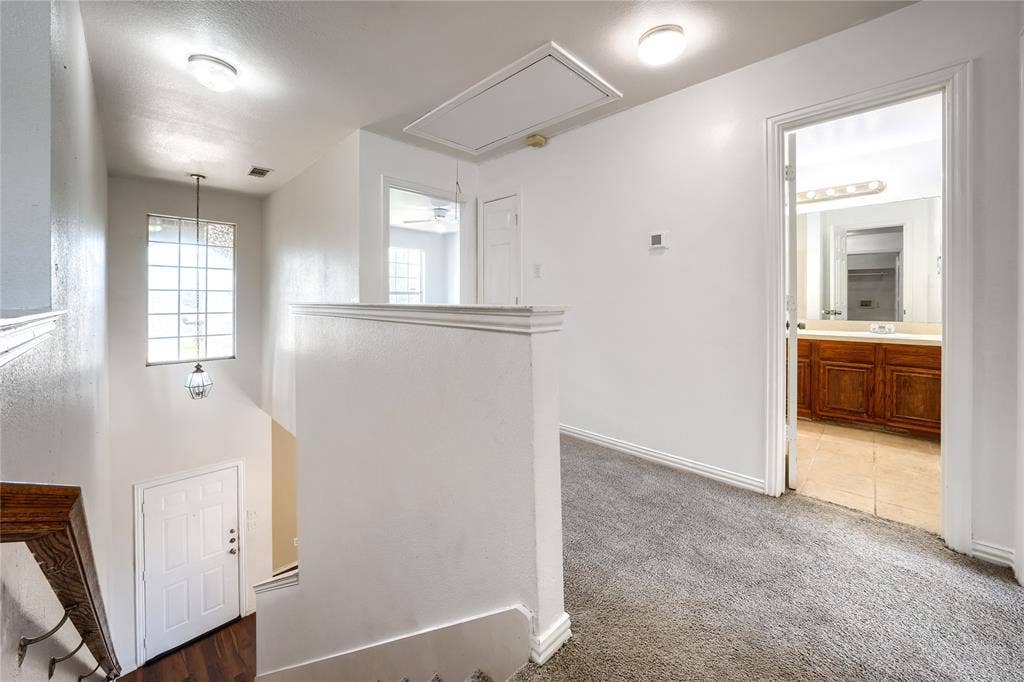 2709 Maci Court, Seagoville, TX 75159 Multi-level interior featuring a carpeted landing, a tall window with grid detailing, a pendant light fixture, and a doorway revealing a bathroom with wood-finish cabinetry