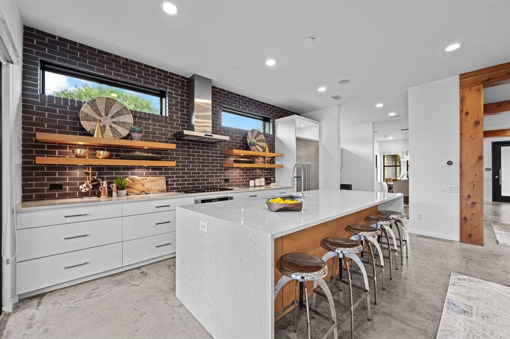 Rich brick, floating wood shelves, and waterfall countertops give the kitchen its distinctive personality.