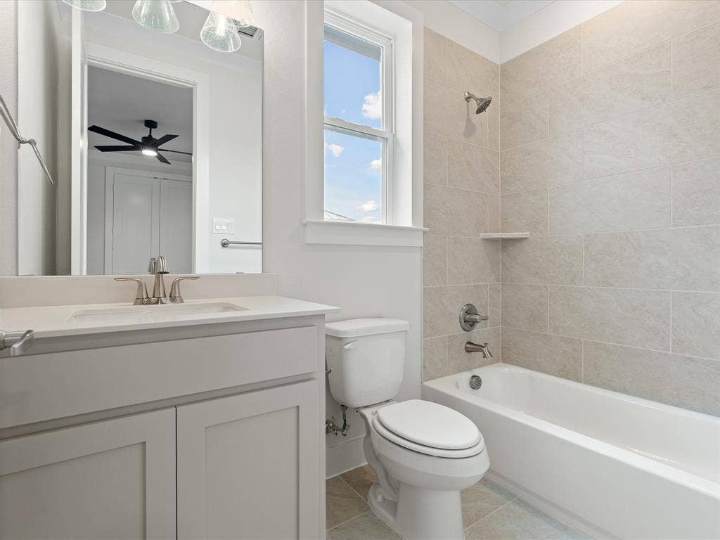 Bathroom featuring a vanity with a white countertop and undermount sink, tiled bathtub surround with a built-in shelf, brushed nickel hardware, and neutral tile flooring