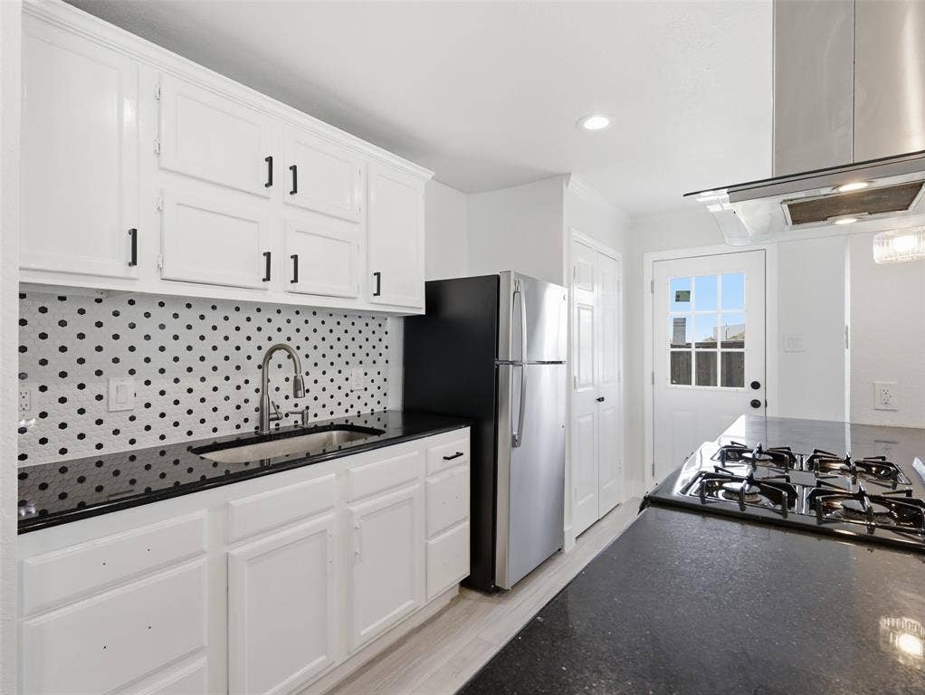 Kitchen featuring white cabinetry, dark countertops, patterned tile backsplash, stainless steel refrigerator, and built-in gas cooktop with stainless steel range hood