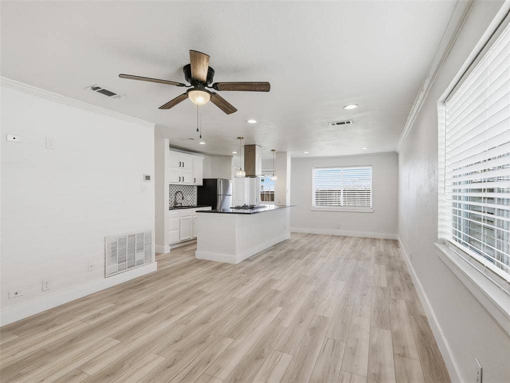 Open-concept interior featuring wood-finish flooring, recessed lighting, a ceiling fan with integrated light fixture, kitchen island with stone-finish countertop, and white cabinetry with a tile backsplash