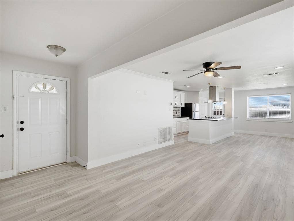 Open-concept interior featuring light wood-finish flooring, recessed lighting, ceiling fans, and a kitchen island with a stainless steel range hood