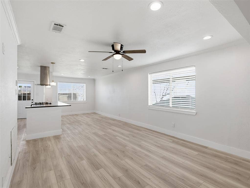 Open interior featuring wood-finish flooring, recessed lighting, a ceiling fan, and a kitchen island with a stone countertop and stainless steel range hood