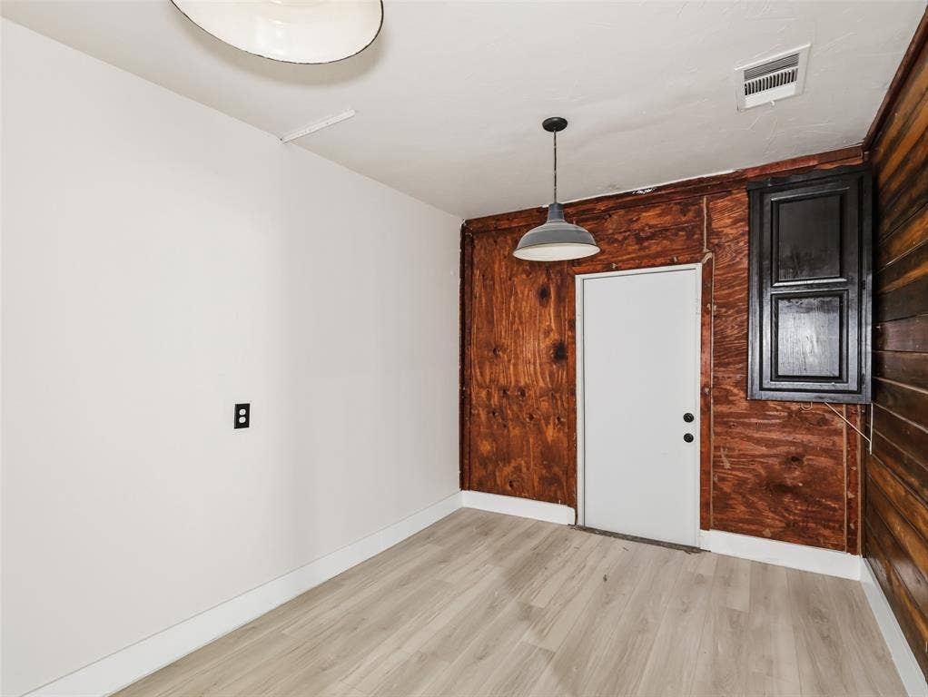 Interior space featuring wood-finish flooring, exposed wood-paneled walls, a single-bulb dome pendant light, and a black-framed window fixture
