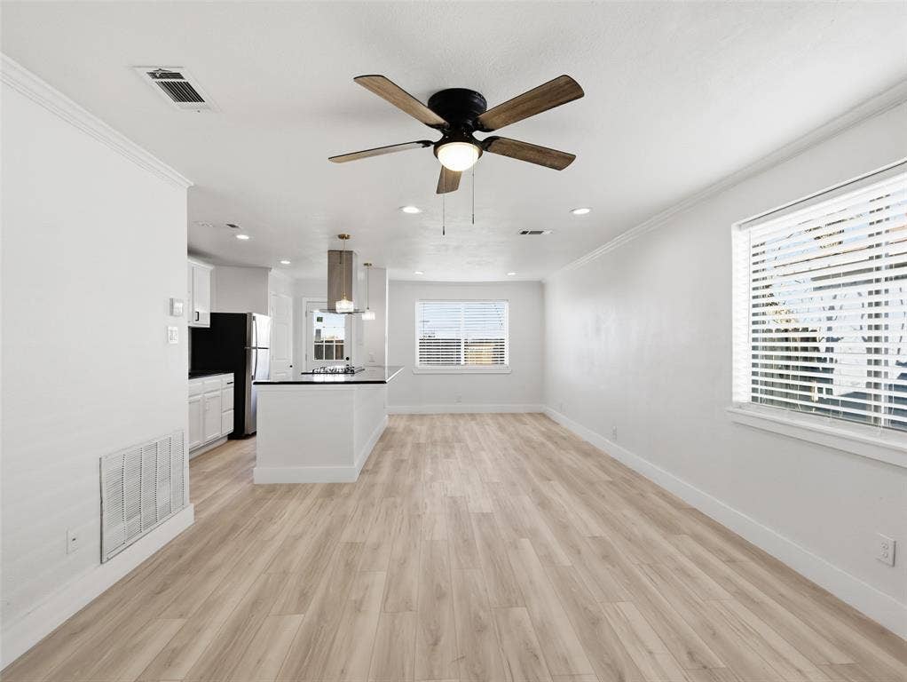 Open-concept interior featuring light wood-finish flooring, recessed lighting, a five-blade ceiling fan, and a kitchen island with a stone countertop