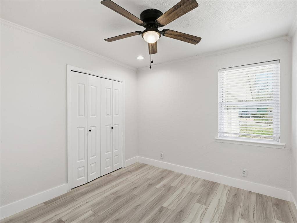 Room featuring wood-finish flooring, a ceiling fan with integrated lighting, bifold closet doors, and a window with horizontal blinds