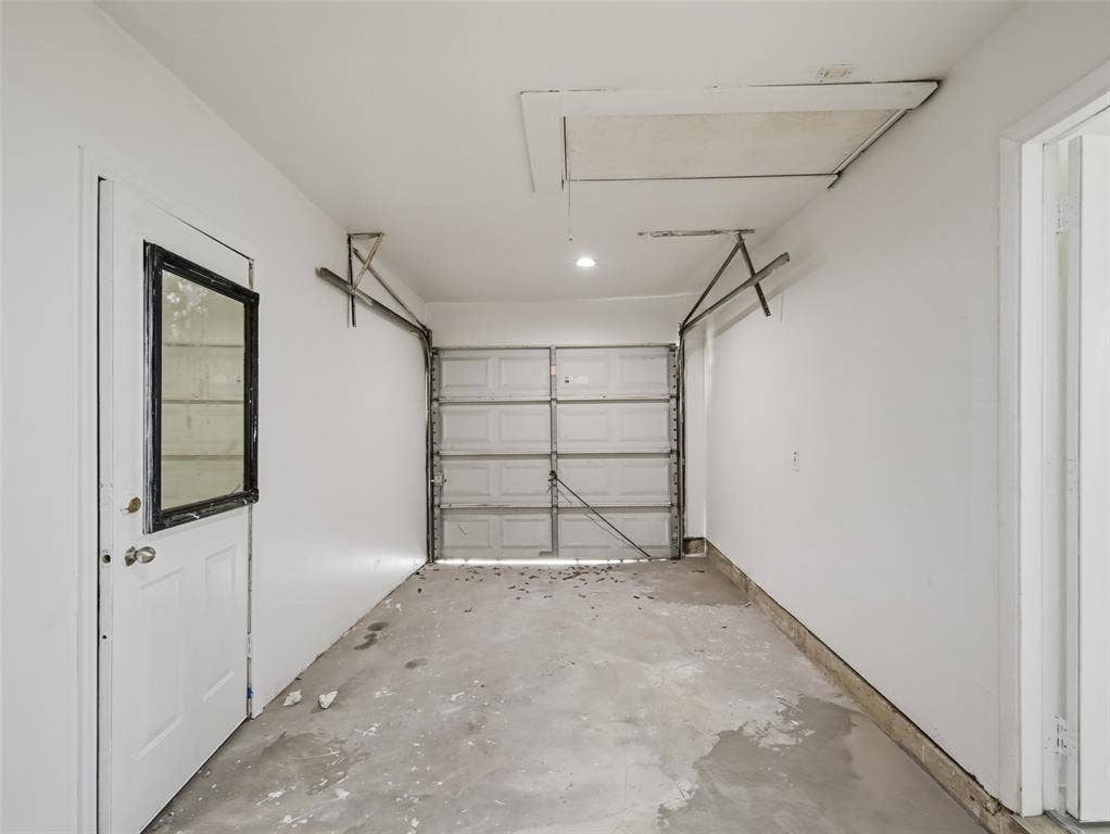 Enclosed garage space featuring a paneled metal overhead door, concrete flooring, and a side access door with a window insert