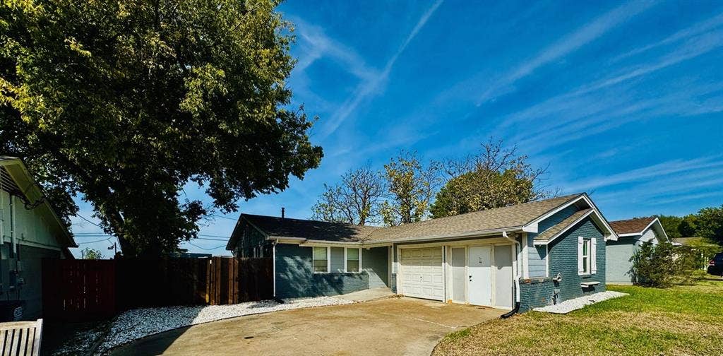 Single-story residence featuring a painted brick exterior, attached garage, concrete driveway, and wooden privacy fencing