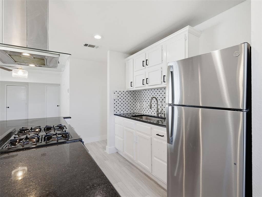 Kitchen featuring white cabinetry, dark stone countertops, stainless steel appliances, a patterned tile backsplash, and wood-finish flooring