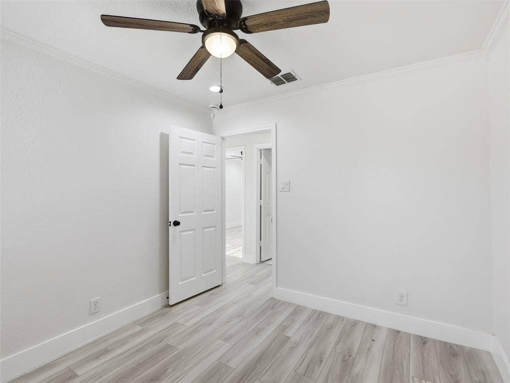 Interior room featuring wood-finish flooring, a multi-blade ceiling fan with integrated light fixture, and a six-panel door