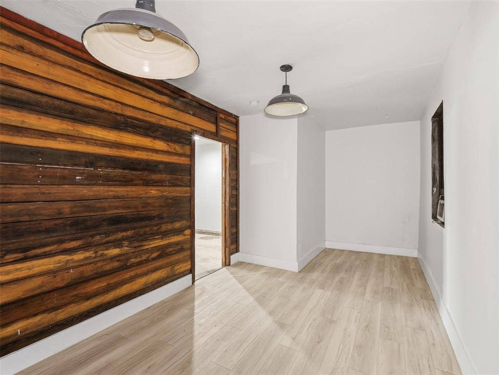 Horizontal wood-plank accent wall, light-toned wood-finish flooring, and dual industrial-style pendant lighting