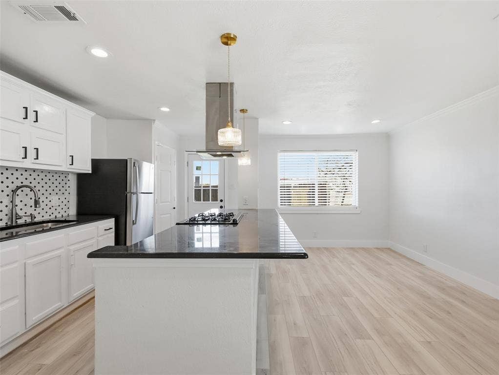 Kitchen featuring white shaker-style cabinetry, dark stone-surface countertops, a center island with an integrated gas cooktop, patterned tile backsplash, and recessed lighting