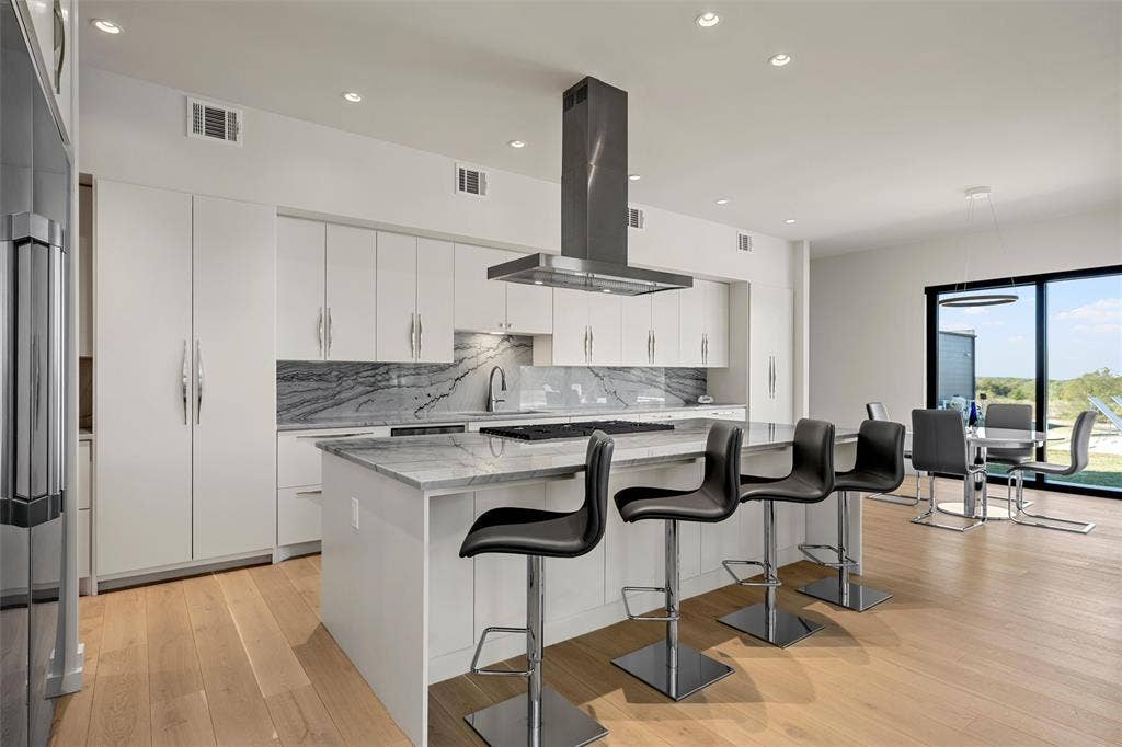 356 Bold Springs Court, West, TX 76691 Gourmet kitchen featuring flat-panel cabinetry, a spacious center island with Quartzite countertops, a stainless steel range hood, and wood flooring