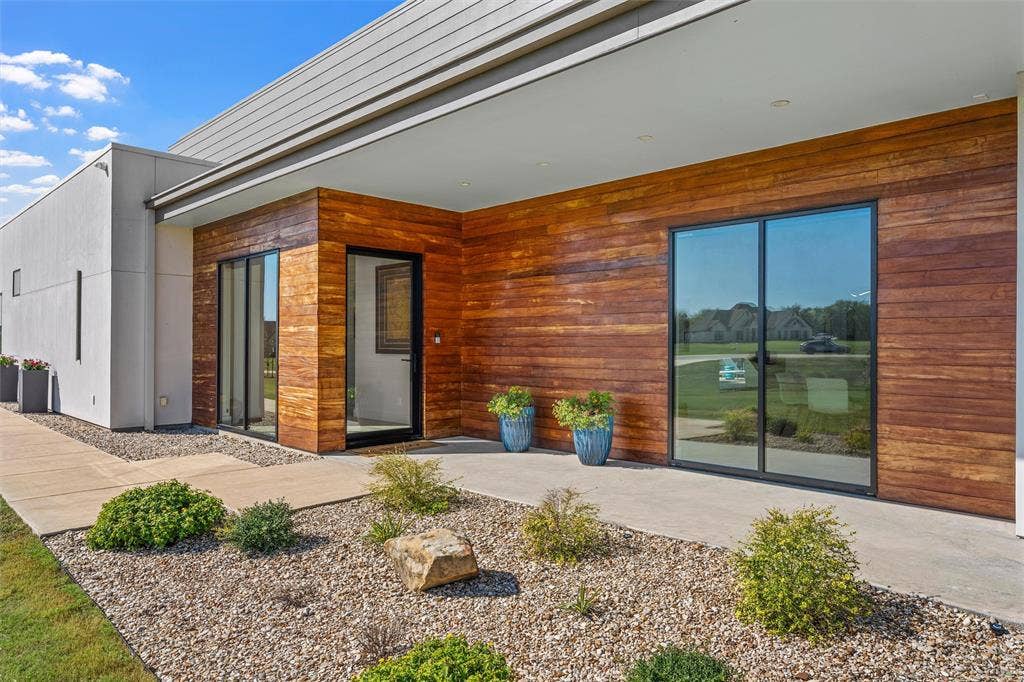 356 Bold Springs Court, West, TX 76691 Contemporary exterior featuring horizontal wood-plank siding, smooth stucco finish, large glass sliding doors, recessed lighting, and a concrete walkway