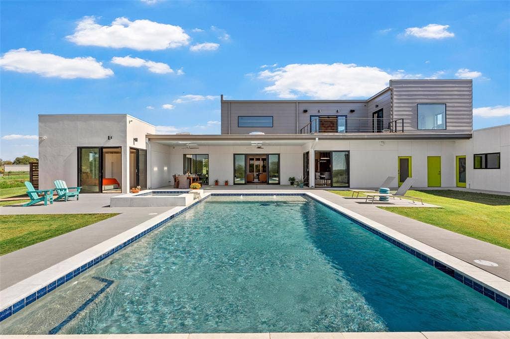 356 Bold Springs Court, West, TX 76691 Contemporary multi-level exterior featuring a rectangular inground pool with an integrated spa, expansive covered patio with skylights, second-story balcony with metal railing, and sleek mixed-material siding