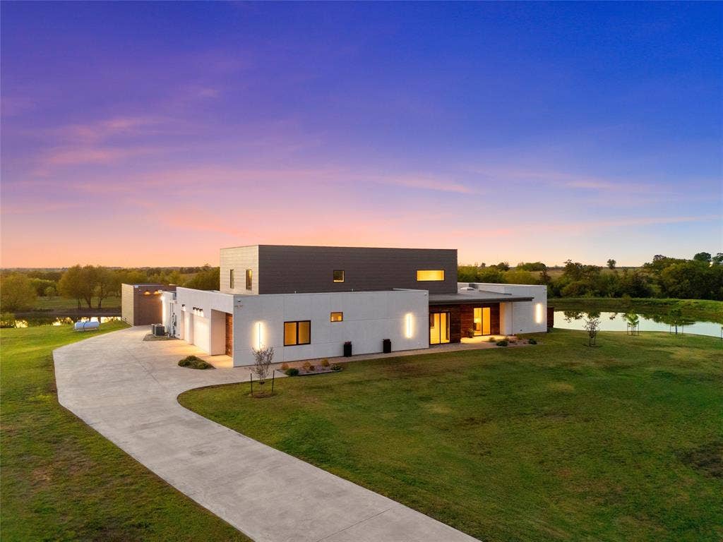 356 Bold Springs Court, West, TX 76691 Modern two-story architectural exterior featuring smooth-finish cladding, expansive concrete driveway, flat roofing, and integrated wall-mounted exterior lighting