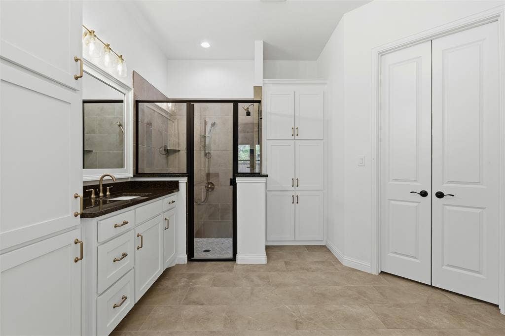 Bathroom featuring white cabinetry, dark countertops, a walk-in shower with a black frame and stone-look tiling, built-in floor-to-ceiling storage, and tile flooring
