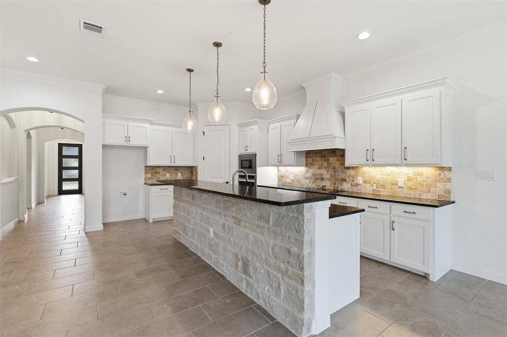 Kitchen featuring white cabinetry, a stone-faced breakfast bar with a dark countertop, a stacked stone backsplash, pendant lighting, and ceramic tile flooring