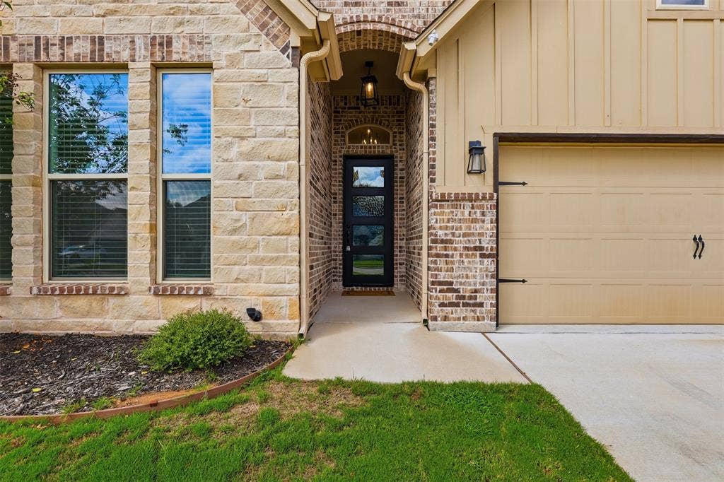 Exterior facade featuring stone masonry, vertical board-and-batten siding, a recessed entryway with a multi-pane glass door, and a multi-section garage door