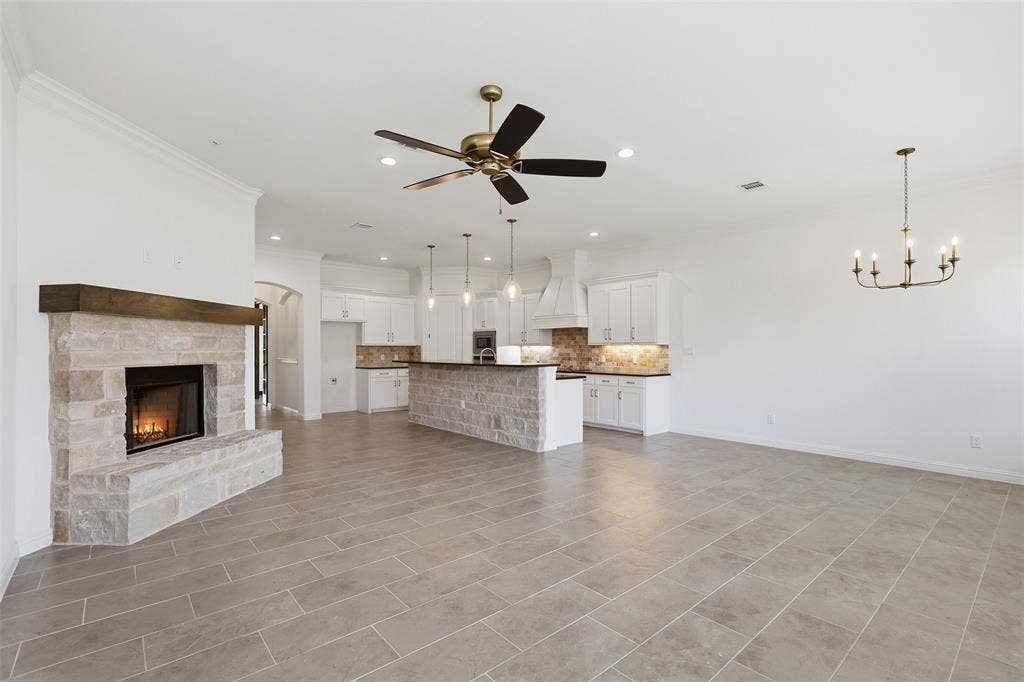 Open-concept area featuring stone-clad fireplace with wood mantel, stone-base kitchen island, custom white cabinetry, recessed lighting, and tile flooring